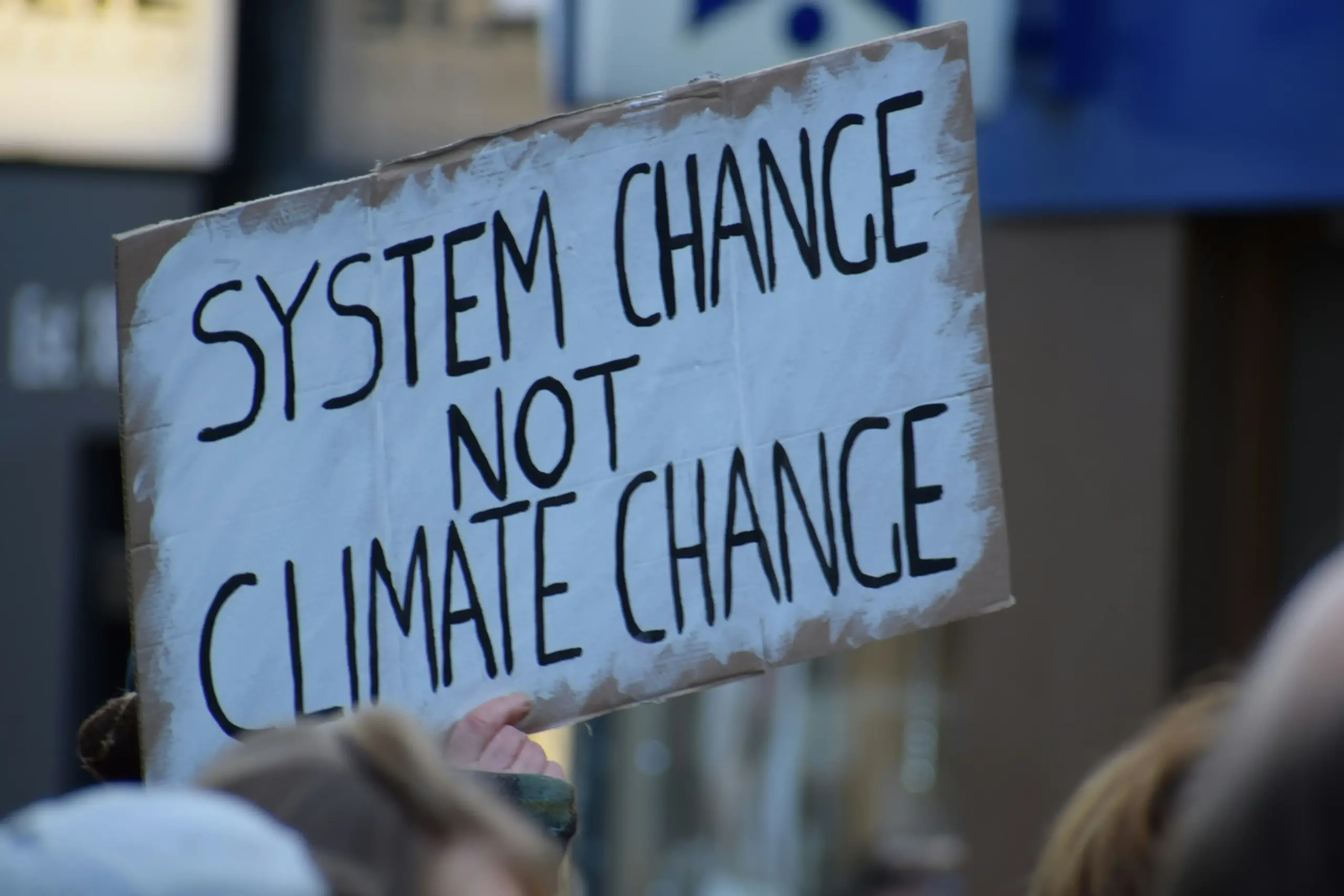 Protest sign on cardboard that says "SYSTEM CHANGE NOT CLIMATE CHANGE"