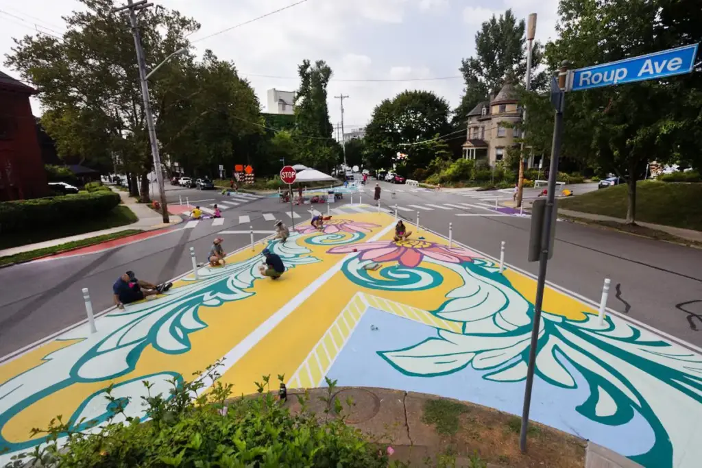 Image of an intersection with beautifully colorful asphalt art, encouraging drivers to slow down and see pedestrians. Asphalt Art Initiative project at Baum Grove in Pittsburgh, PA. Mural by Tim Engelhardt and Randi Stewart with Friendship Community Group.