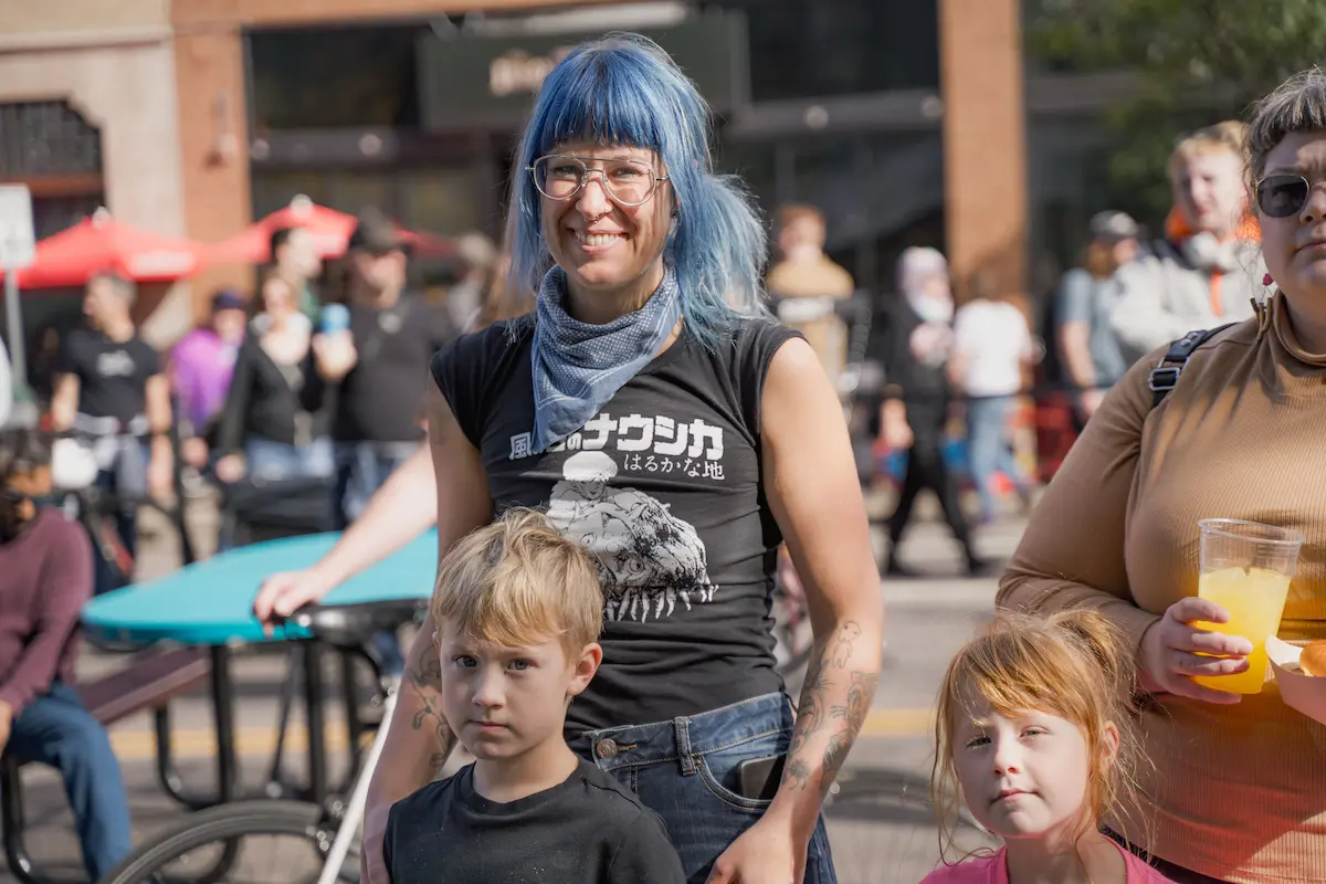person with fun blue hair smiling with their kids at Open Streets