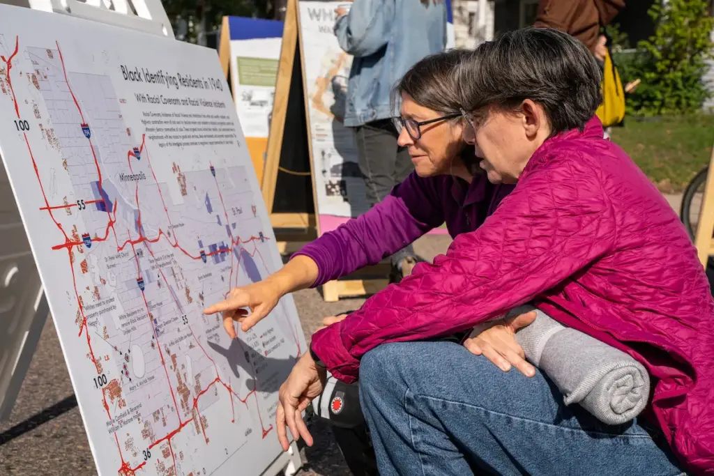 Two people looking at a map of highways routed through marginalized neighborhoods during a community event
