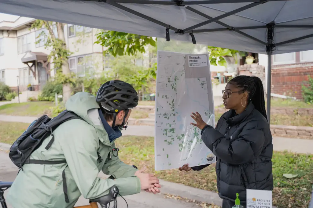 person showing racial covenants on a map of Minneapolis to someone wearing a bike helmet at Open Streets