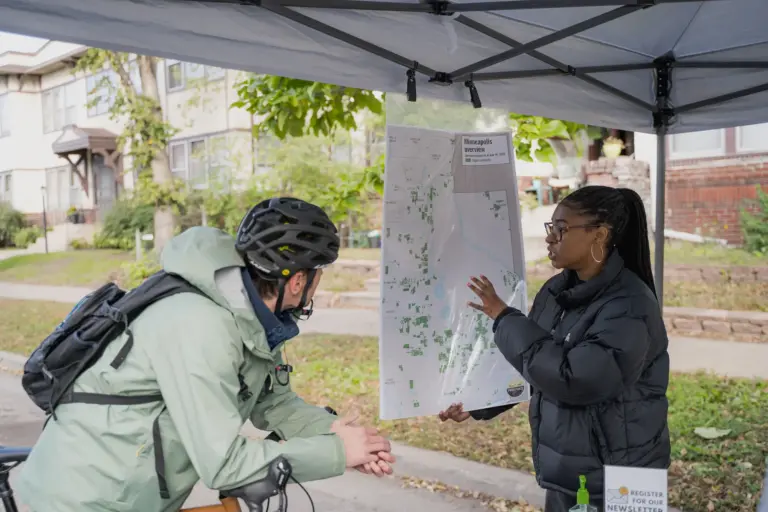 person showing racial covenants on a map of Minneapolis to someone wearing a bike helmet at Open Streets