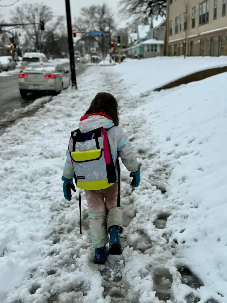 small child walking with backpack though unplowed sidewalk
