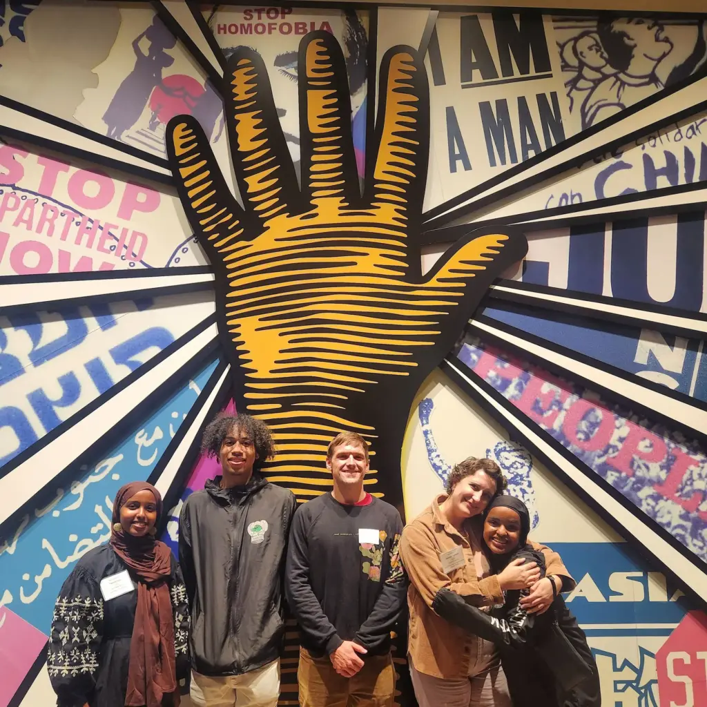 group of people posing in front of large hand mural