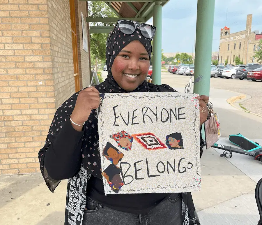 person smiling with "everyone belongs" on a quilt square from a community event