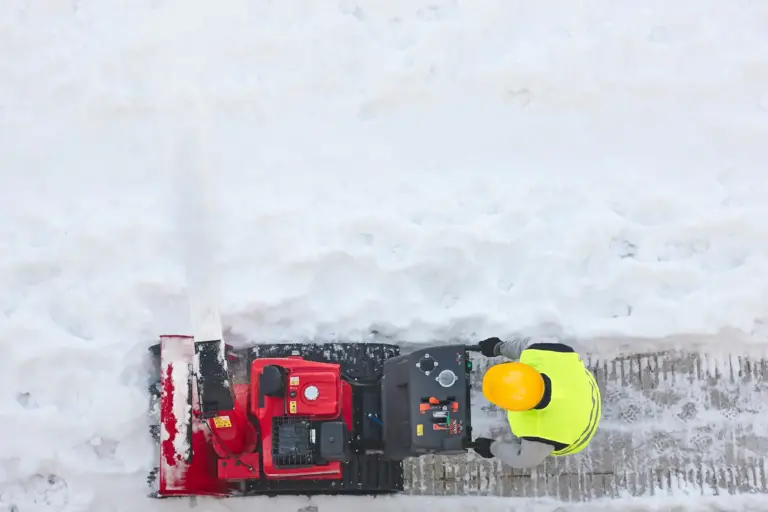 Aerial shot of a person using a motorized plowing machine to clear snow on the sidewalk.