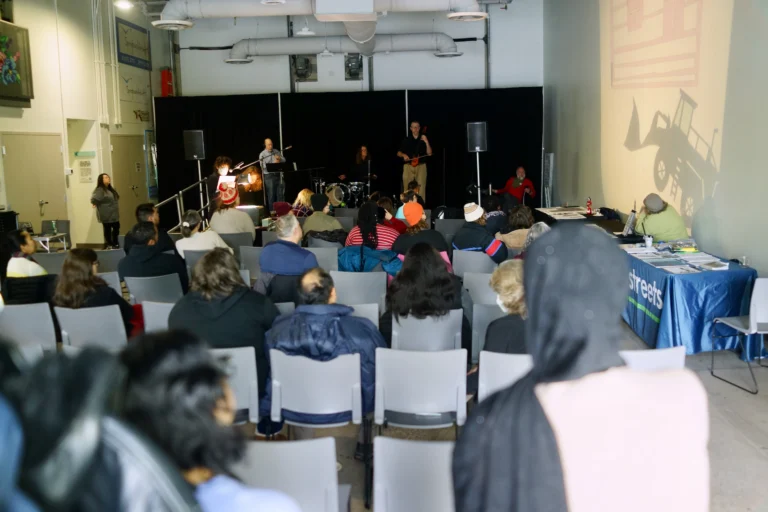 Audience members watching the big screen with the puppet show, "How'd We Get Here" and the band Sonoglyph Collective playing.
