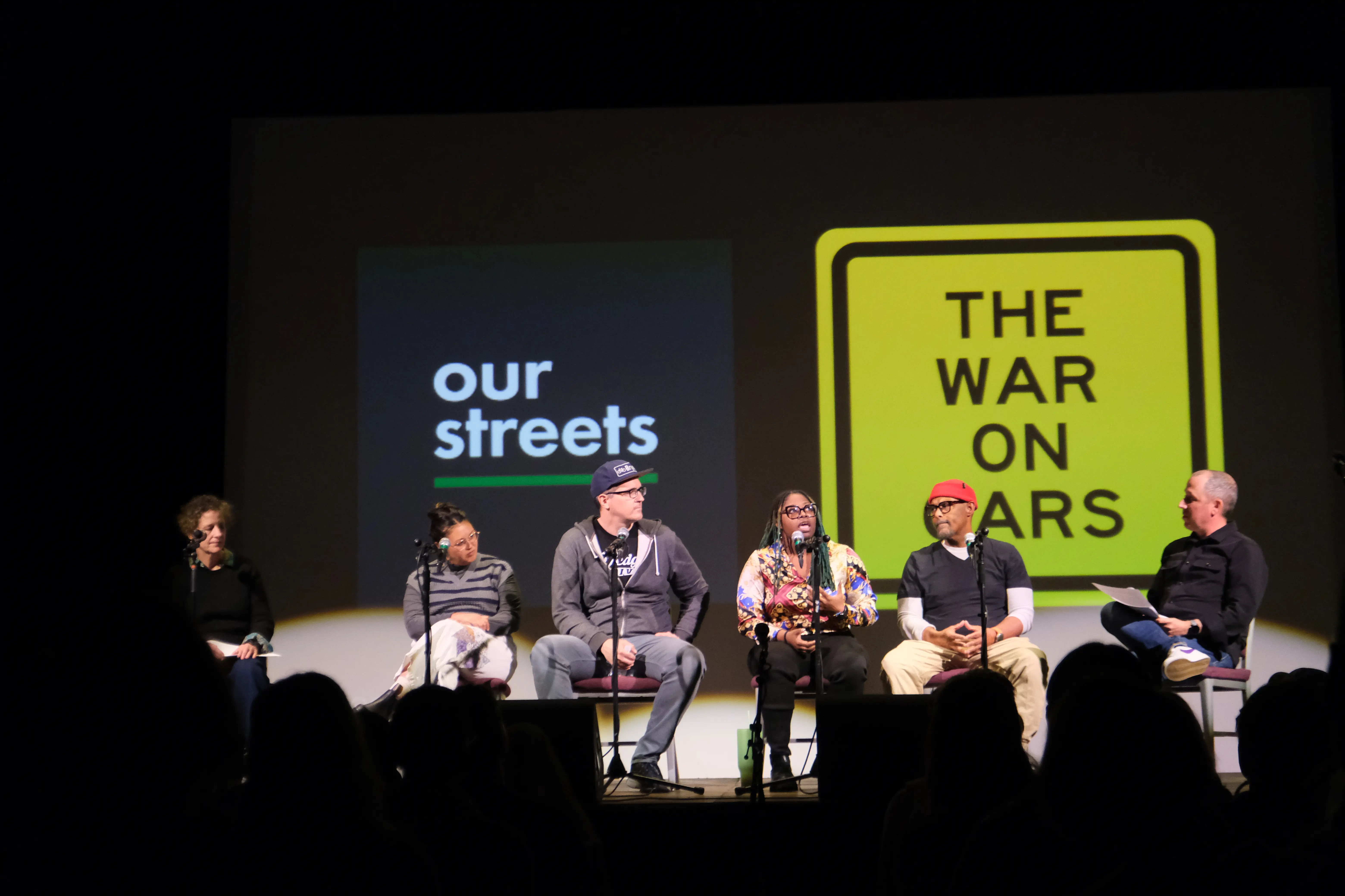 People seated panel-style on stage with the Our Street and The War on Cars logos projected