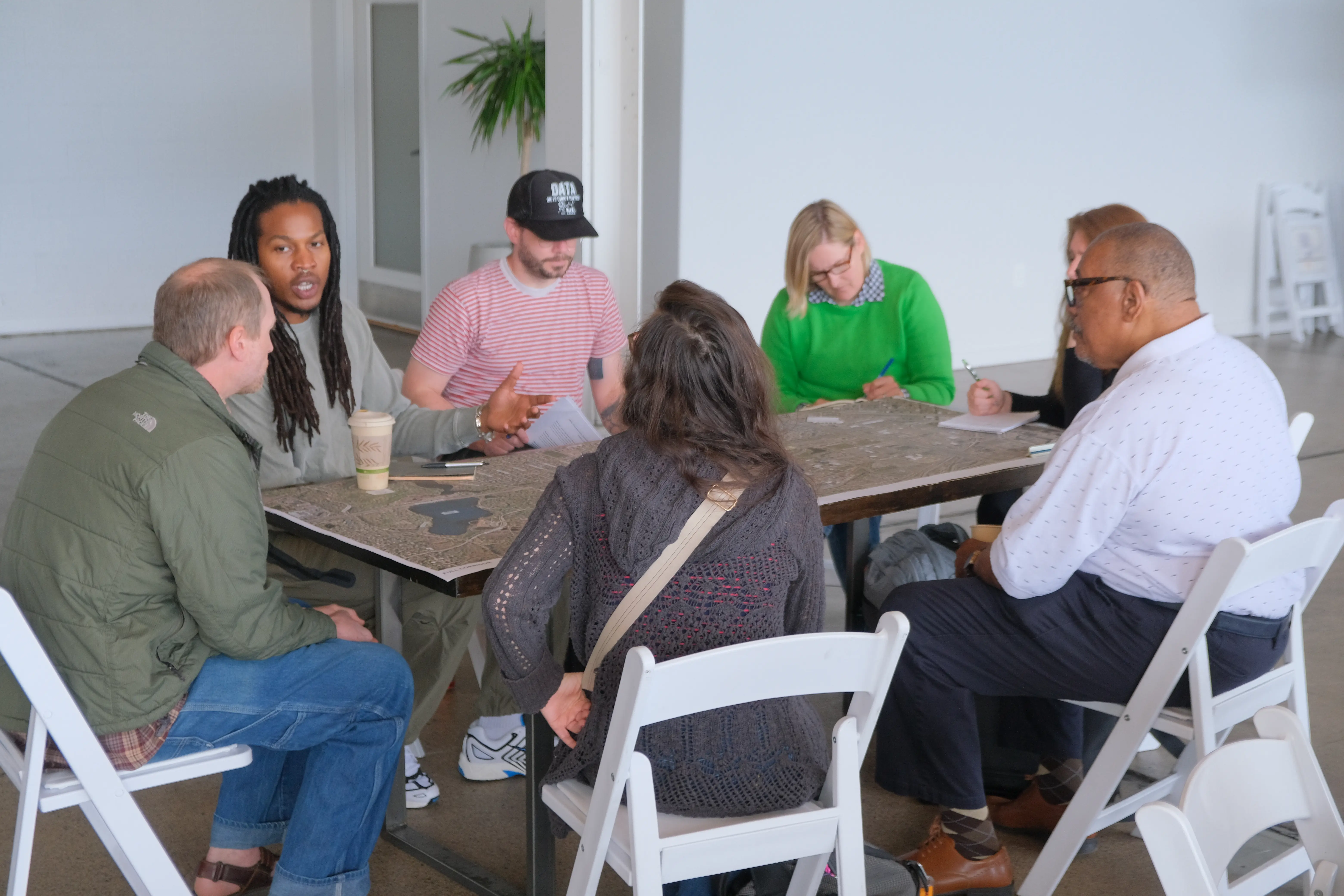 Group of people at a table talking with a big aerial map of the Olson Memorial Highway corridor.